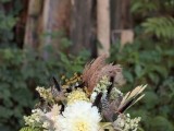 a fall woodland wedding bouquet of white blooms, feathers, ferns and greenery and grasses