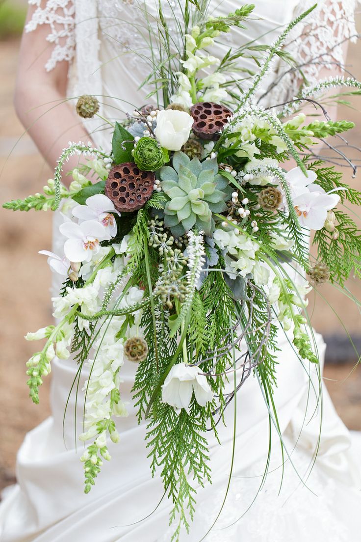 A bold cascading wedding bouquet of various types of greenery, a succulent, white orchids and lotus is great for a woodland wedding