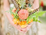 a colorful woodland wedding bouquet with orange and coral blooms, greenery and feathers is a unique option with plenty of color