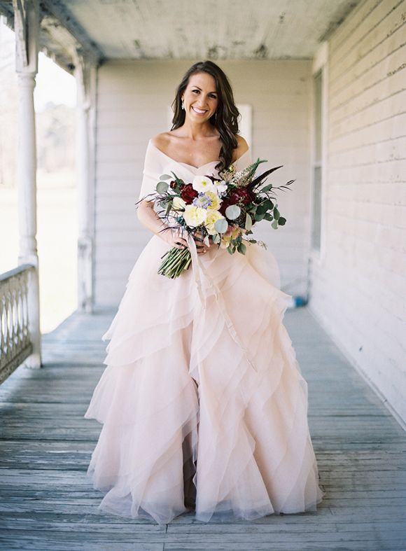 A glam and romantic blush strapless wedding dress with a layered skirt with ruffles and a coverup