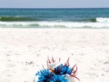 a bright beach wedding bouquet of bright blue and white flowers and red feathers is a bright look