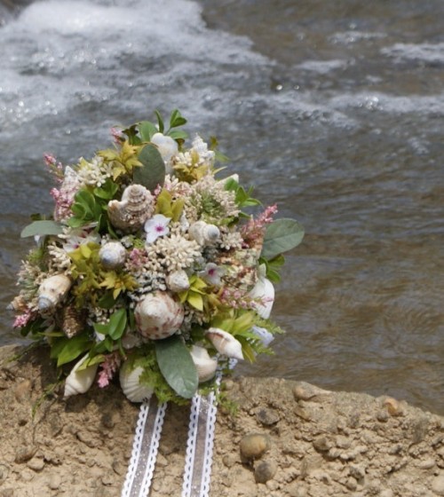 a simple beach wedding bouquet with white blooms, greenery and some seashells plus white ribbons