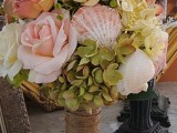 a beach wedding bouquet of neutral and pink blooms, greenery and pink seashells looks very natural