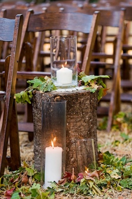 fall wedding aisle decor with a tree stump, leaves, candles and greenery on the stump and on the ground