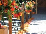 a bright fall wedding aisle with orange and yellow blooms and greenery plus super colorful fall leaves on the ground is amazing