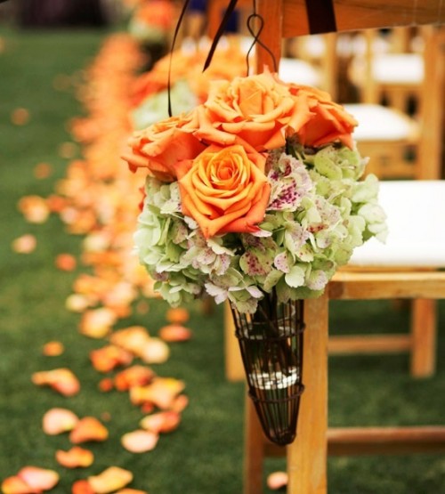a bright fall wedding aisle arrangement of green hydrangeas and orange roses plus orange petals on the ground is amazing