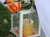 a candle lantern with an orange candle and orange roses is a chic and elegant idea to decorate the wedding aisle