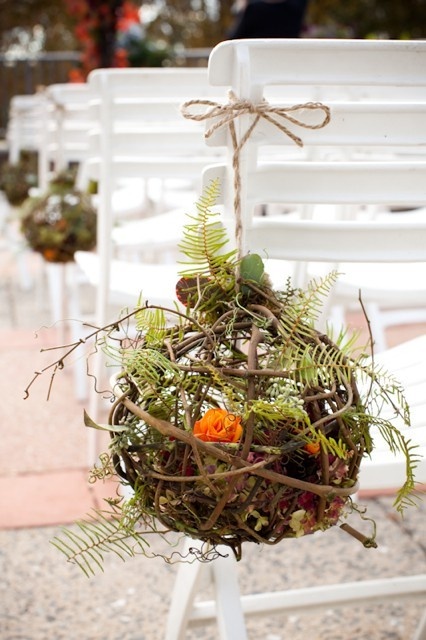 a twig ball with greenery and fern plus orange roses inside is a very cool and bright idea for a fall woodland wedding
