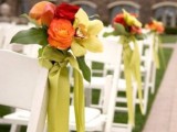 a bold fall wedding aisle decoration of green, orange and red blooms and greenery, green ribbons is a very bold and cool idea