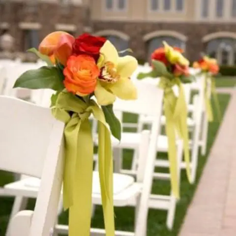 a bold fall wedding aisle decoration of green, orange and red blooms and greenery, green ribbons is a very bold and cool idea