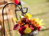 a bold fall wedding aisle decoration of burgundy, deep red, orange and yellow blooms in a jar is a very cool and fresh idea to rock