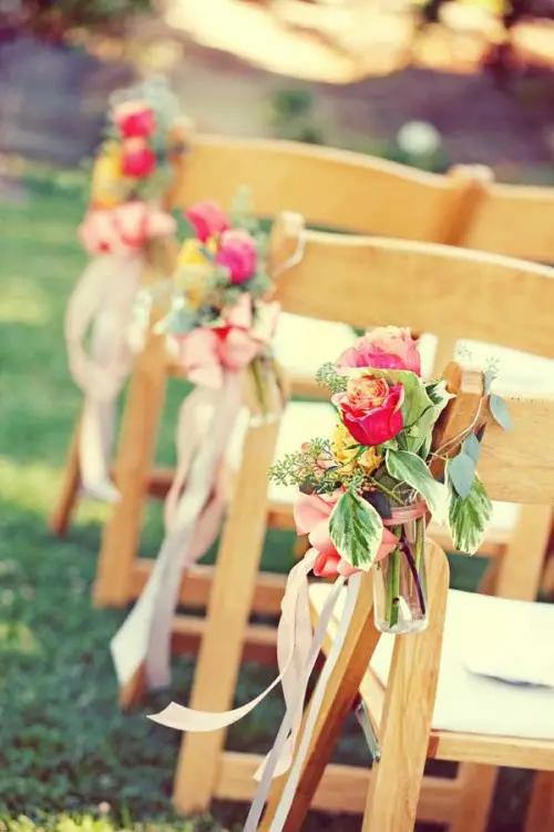 a bold fall wedding aisle arrangement of pink and yellow roses, greenery and pink ribbons is a lovely idea for the fall