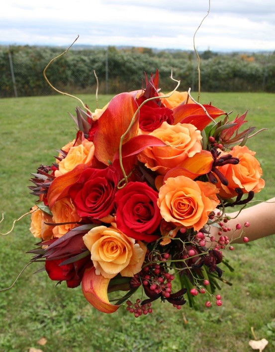 A colorful fall wedding bouquet of orange, red and burgundy blooms, berries, greenery and twigs is a very catchy and bold idea