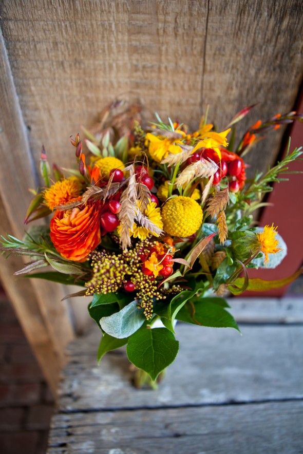 A bright wedding bouquet of orange and yellow blooms, billy balls, cranberries and wheat and greenery is a very cool idea for a rustic fall bride