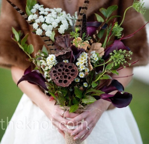 a bold and contrasting fall wedding bouquet of deep purple callas, white blooms, greenery and feathers and lotus slices is a cool idea for a moody fall wedding