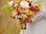 a bright and lively fall wedding bouquet of white, yellow and blush blooms, berries, greenery and bright fall leaves plus ribbons is a cool idea for a fall wedding