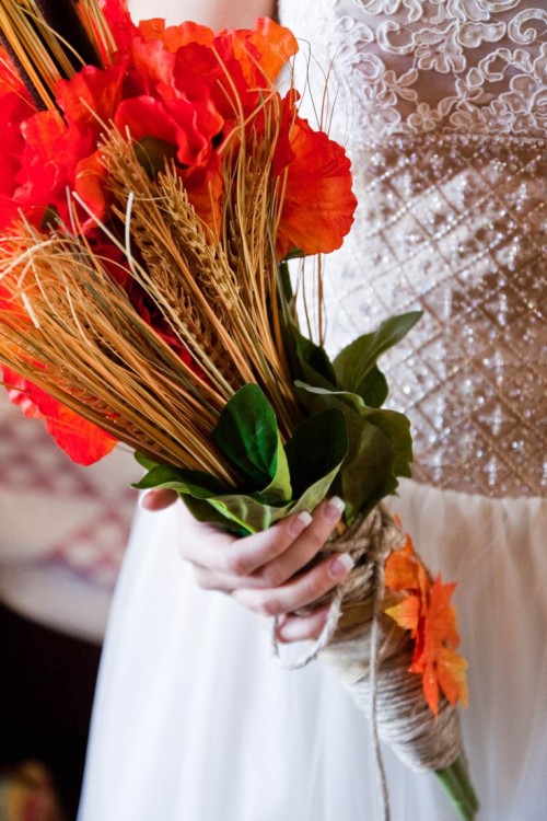 a catchy and colroful wedding bouquet of deep red and orange blooms, wheat and some greenery, a yarn wrap and some faux fall leaves is a cool idea for a rustic bride