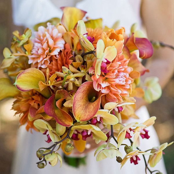 A fall colored wedding bouquet of yellow, rust, orange and pink blooms, some greenery and twigs is amazing for the fall