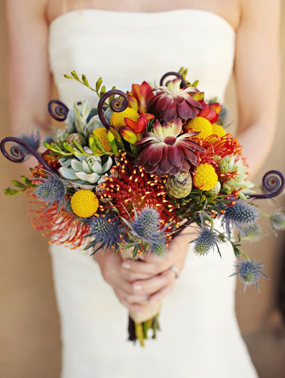 A colorful fall wedding bouquet of burgundy and rust blooms, thistles, billy balls, succulents and lotus is an eye catchy idea to try