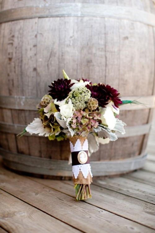 a contrasting fall wedding bouquet of deep purple and white blooms, pale foliage, seed pids and a burlap wrap is a great and non-typical idea for a fall rustic wedding