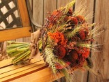a rustic fall wedding bouquet of bold orange and rust blooms, wheat and some berries plis a brown ribbon bow is a cool idea to rock