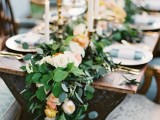 a lush eucalyptus table runner with peachy pink blooms and tall candles is a refined idea to try