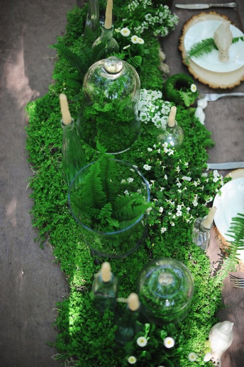a moss and fern table runner with tiny white blooms and candles is a gorgeous idea for a woodland wedding