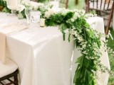 a greenery and white bloom table runner going to the floor, white blooms match white candles