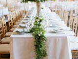 a delicate greenery and white flower table runner and a matching large centerpiece in a vase