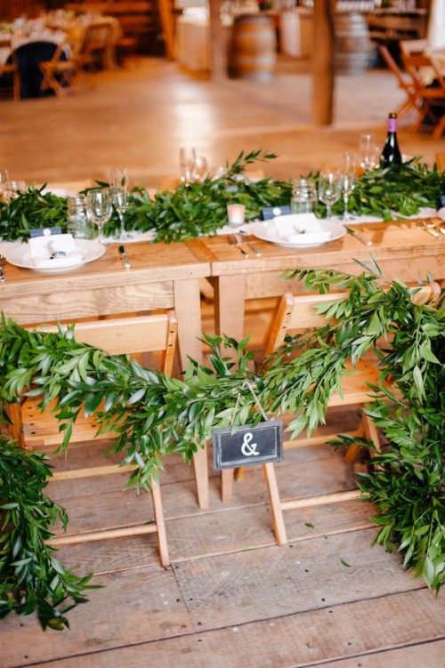 a foliage table runner and a matching garland on the chairs is a chic idea for a rustic space