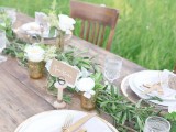 a greenery table runner and white blooms in vases and jars for a cozy rustic table setting