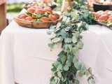 a eucalyptus table runner over a white tablecloth is a chic and timeless idea