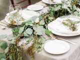 a simple greenery table runner and a grey tablecloth is a cool and very neutral idea