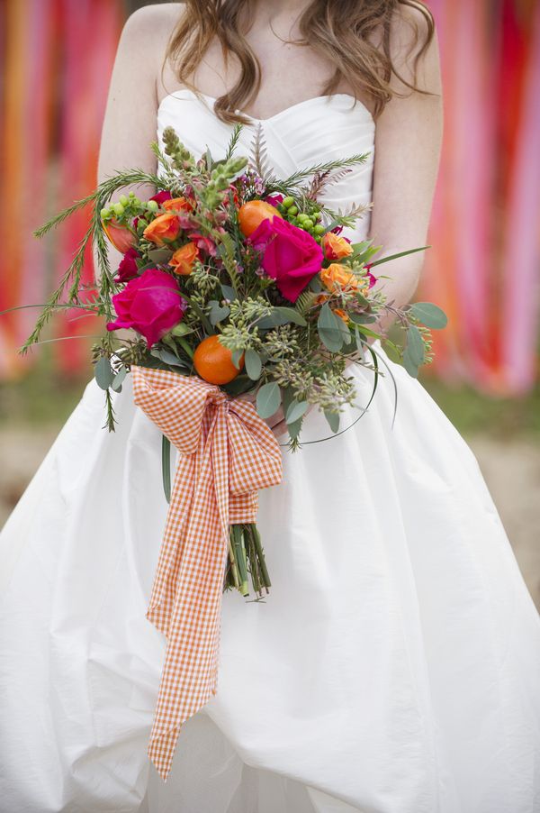 A bright and whimsical wedding bouquet of yellow, fuchsia blooms, messy greenery and some citrus plus a large plaid bow is a statement and real chic