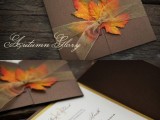 a brown wedding invitation suite done with bright fake fall leaves and some sheer ribbon for a fall wedding