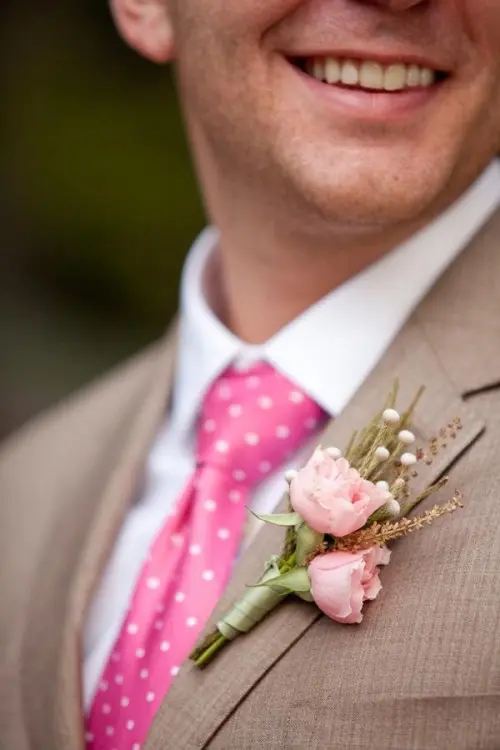 a light brown suit with a pink polka dot tie, a floral boutonniere and a white shirt