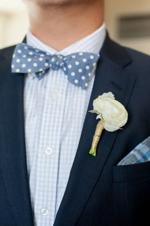 a bold look with a touch of whimsy, a navy suit, a plaid light blue shirt and a blue polka dot bow tie