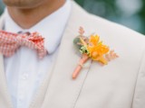 a creamy groom’s three-piece suit with a white shirt, an orange plaid bow tie and orange boutonniere