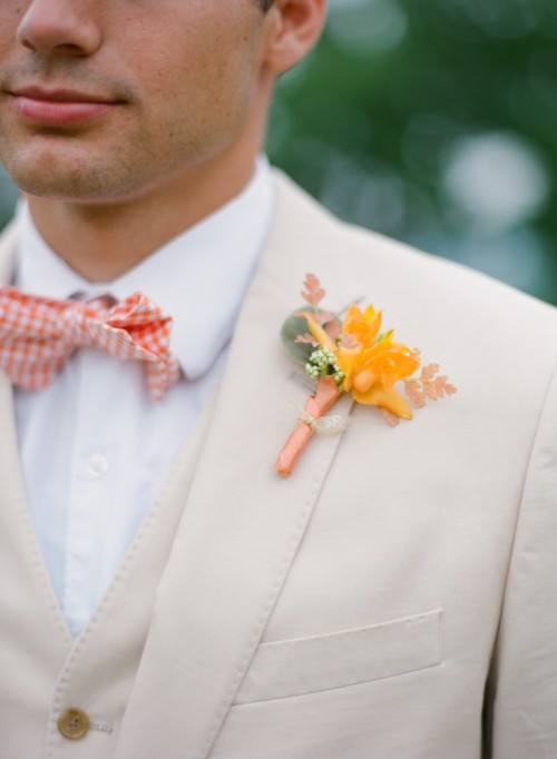 a creamy groom's three-piece suit with a white shirt, an orange plaid bow tie and orange boutonniere