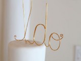 a sleek white wedding cake topped with a gold wire topper is a stylish idea for a minimalist wedding