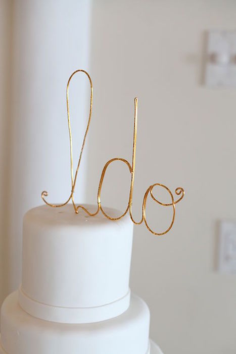 a sleek white wedding cake topped with a gold wire topper is a stylish idea for a minimalist wedding