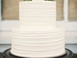 a white textural buttercream wedding cake topped with white blooms and greenery