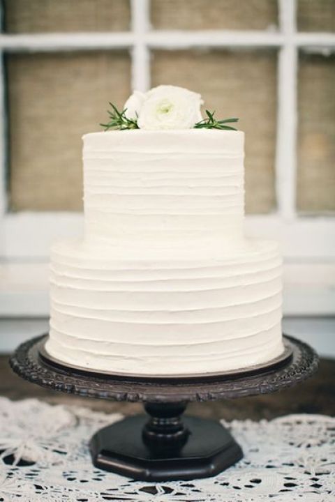 a white textural buttercream wedding cake topped with white blooms and greenery