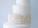 an airy minimalist wedding cake in white and neutrals with a textural tier and a sugar bloom on top