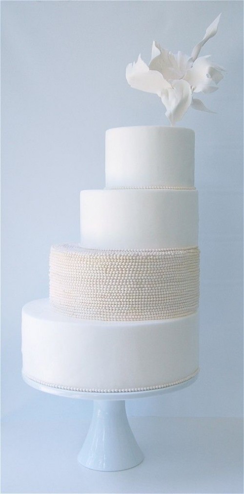 an airy minimalist wedding cake in white and neutrals with a textural tier and a sugar bloom on top