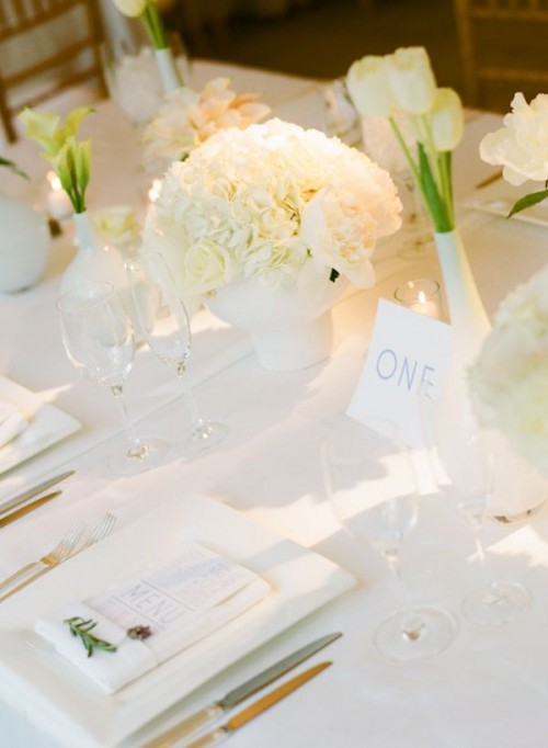 a neutral minimalist wedding tablescape with white bloomsin matte white vases and white candles