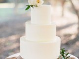 a minimalist white wedding cake topped with neutral blooms and some foliage