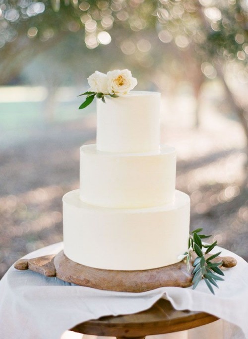 a minimalist white wedding cake topped with neutral blooms and some foliage