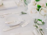 a minimalist neutral tablescape with a neutrla floral centerpiece, menus and white pillar candles