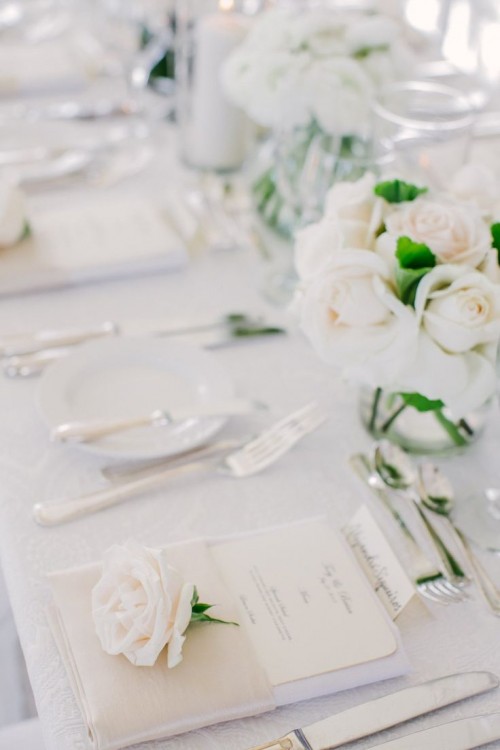 a minimalist neutral tablescape with a neutrla floral centerpiece, menus and white pillar candles